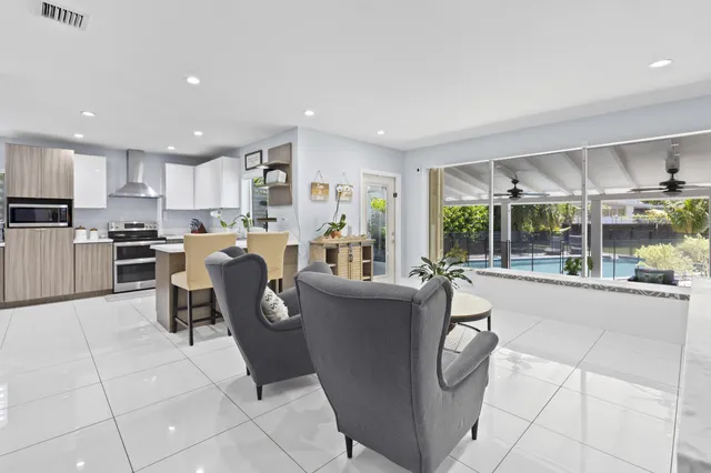 a living room with stainless steel appliances furniture a rug kitchen view and a large window