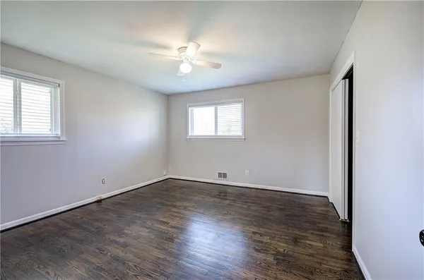 an empty room with wooden floor chandelier fan and windows