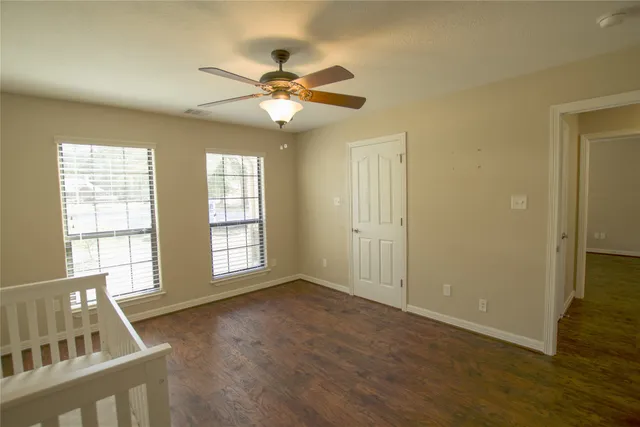 an empty room with wooden floor fan and windows