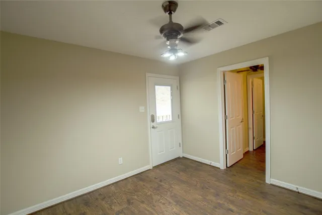 a view of an empty room with wooden floor and a ceiling fan
