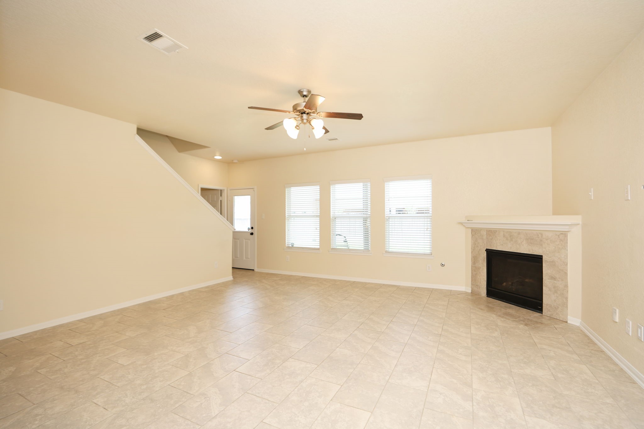 18402 Spruce Tree Line Trail Houston, TX 77084 - Photo 3 of 30 This spacious living room features a tiled floor, ceiling fan, and a cozy corner fireplace. It has large windows for natural light and an adjacent staircase leading upstairs.