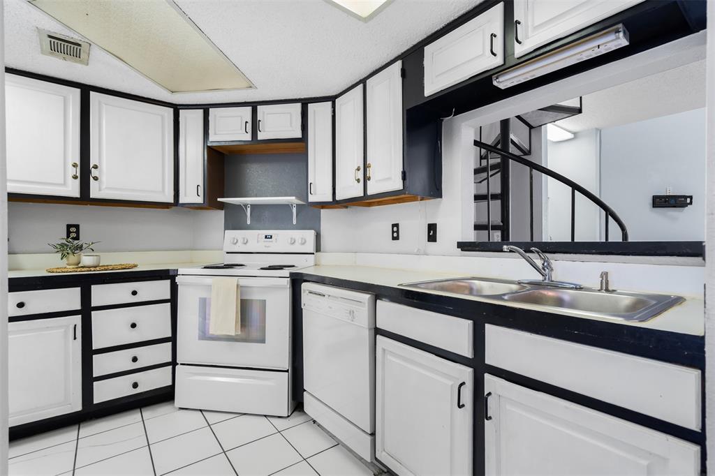 5590 Spring Valley Road, Unit H 203 Dallas, TX 75254 - Photo 10 of 27 Kitchen featuring white cabinetry with black trim, white appliances including a range and dishwasher, a double basin stainless steel sink, and white tile flooring