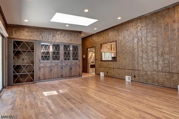 an empty room with wooden floor and way to kitchen