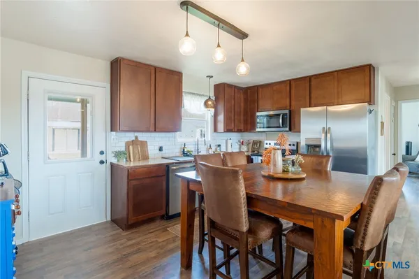 a kitchen with stainless steel appliances granite countertop a kitchen island a stove a refrigerator a sink a dining table and chairs with wooden floor