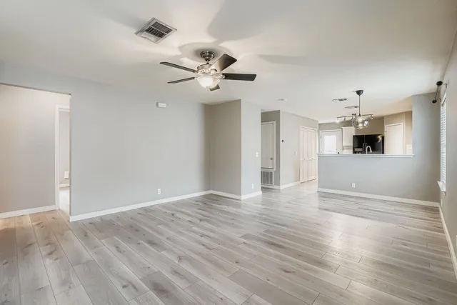 a view of an empty room with wooden floor and a ceiling fan