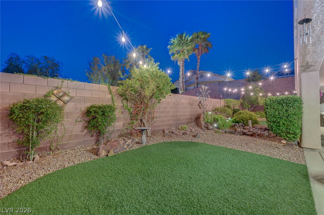 1604 Cattle Ranch Place Henderson, NV 89002 - Photo 94 of 99 A well-landscaped backyard featuring artificial turf, decorative string lights, and mature palm trees.
