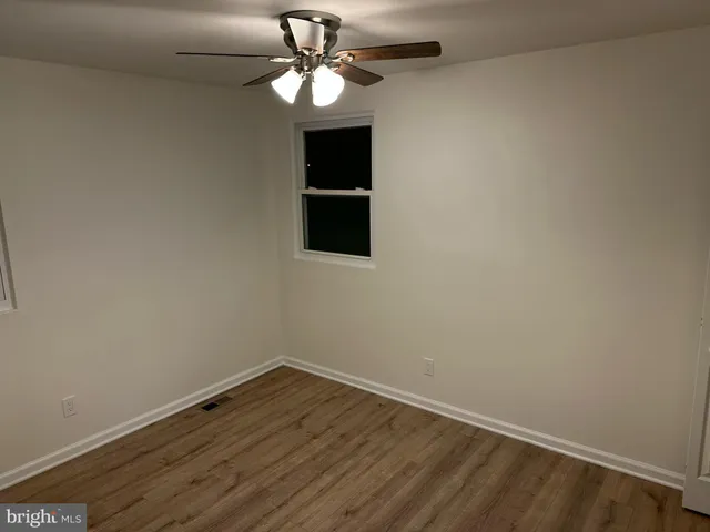 an empty room with wooden floor chandelier fan and windows
