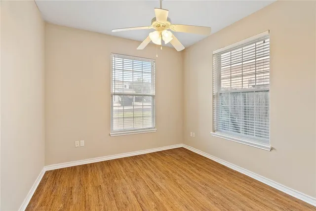 an empty room with wooden floor chandelier fan and windows