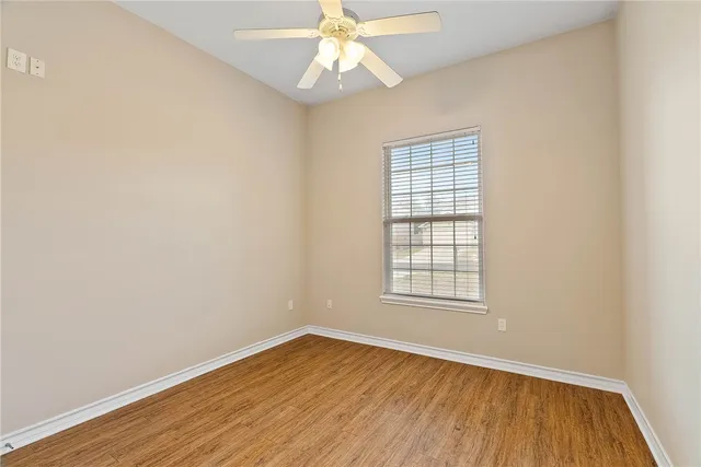 an empty room with wooden floor chandelier fan and windows