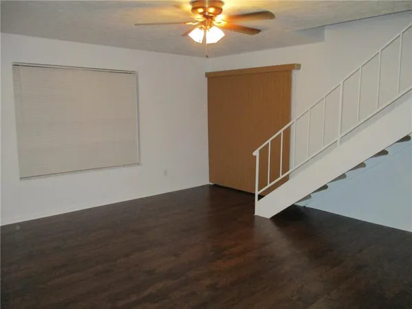 a view of an empty room with wooden floor and a ceiling fan