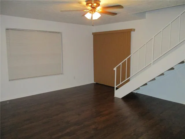 a view of an empty room with wooden floor and a ceiling fan