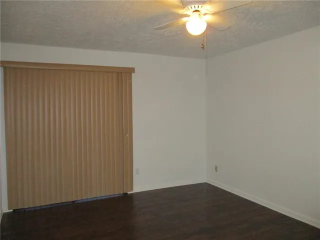 an empty room with a chandelier fan and wooden floor