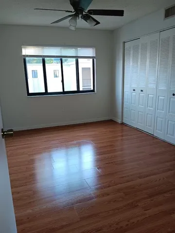 an empty room with wooden floor chandelier fan and windows