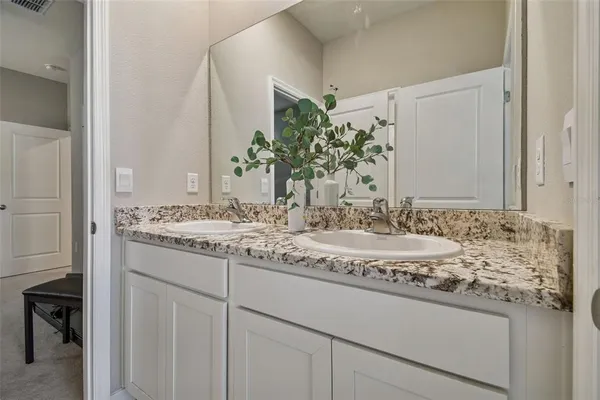 an empty room with chandelier fan and kitchen view