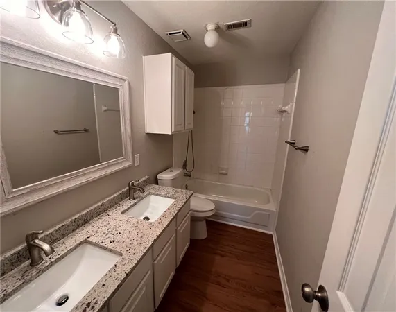 a bathroom with a granite countertop double vanity sink a mirror and a bathtub