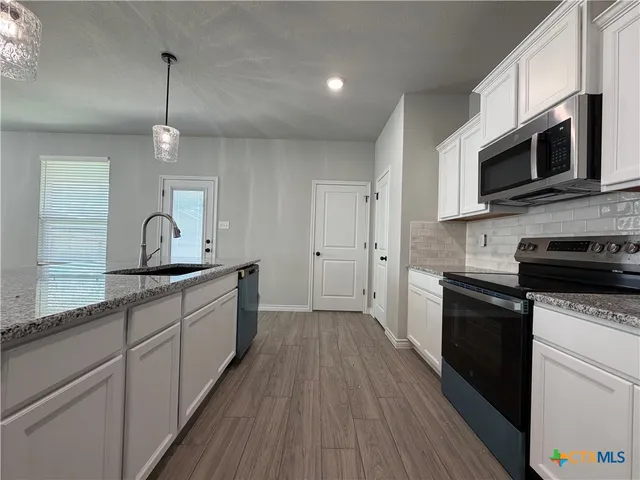 a kitchen with stainless steel appliances granite countertop a sink a stove top oven and wooden floors