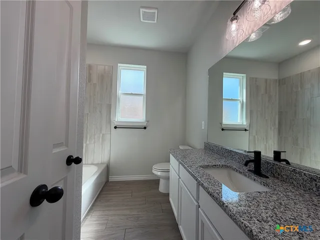 a bathroom with a granite countertop sink a toilet and mirror