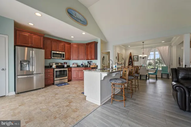 a kitchen with stainless steel appliances kitchen island granite countertop a refrigerator a stove a sink a dining table and chairs with wooden floor