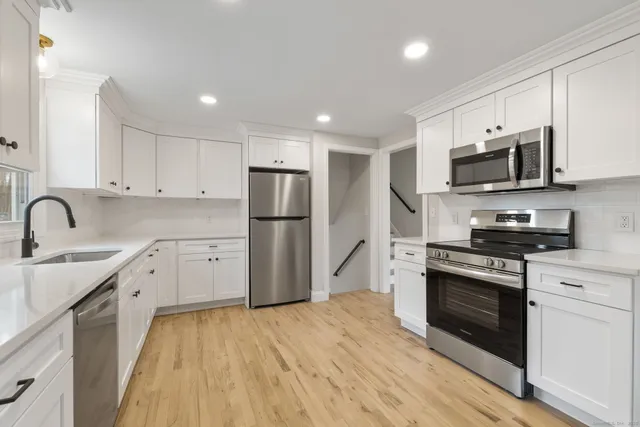 a kitchen with stainless steel appliances a refrigerator stove a sink and white cabinets