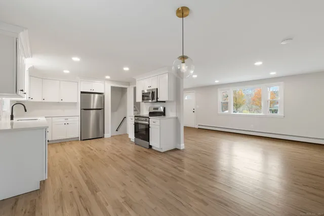 a kitchen with stainless steel appliances kitchen island granite countertop a refrigerator a sink dishwasher a stove and white cabinets with wooden floor