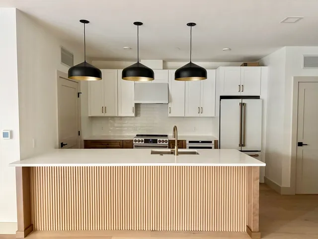 a kitchen with stainless steel appliances granite countertop white cabinets a refrigerator a sink a stove and a wooden floors