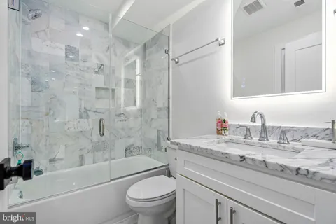 a bathroom with a granite countertop bathtub shower sink vanity mirror and toilet