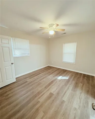 an empty room with wooden floor fan and windows
