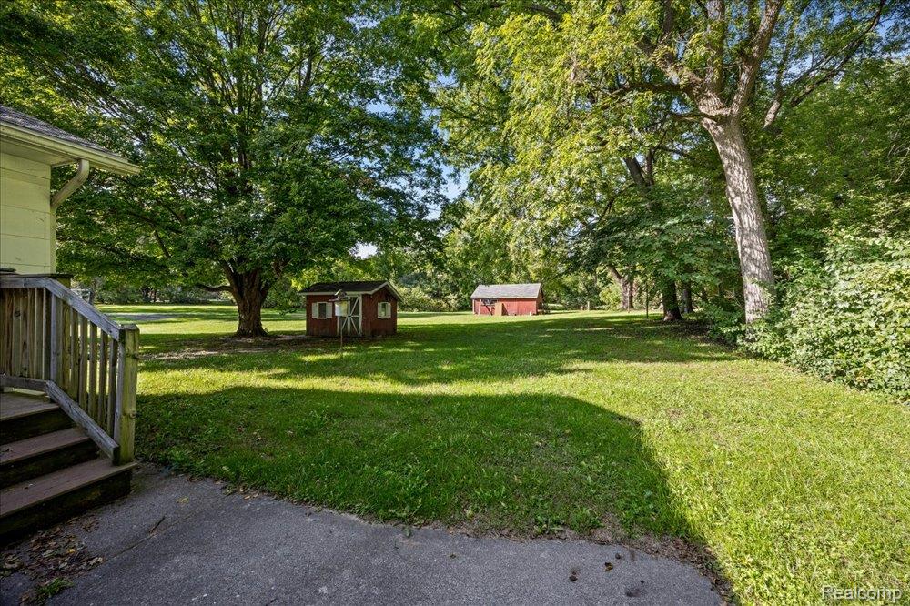 59380 10 Mile Road South Lyon, MI 48178 - Photo 37 of 53 Expansive green lawn with mature trees and two red storage sheds