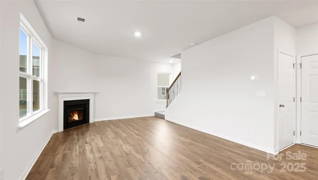 a view of an empty room with wooden floor fireplace and a window