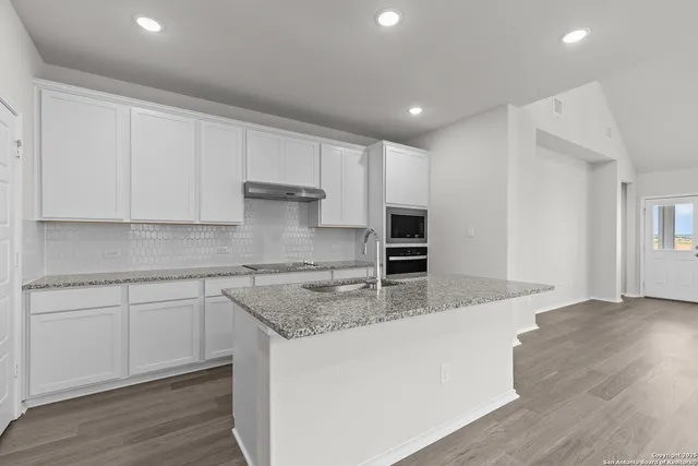 a kitchen with kitchen island granite countertop a sink cabinets and wooden floor