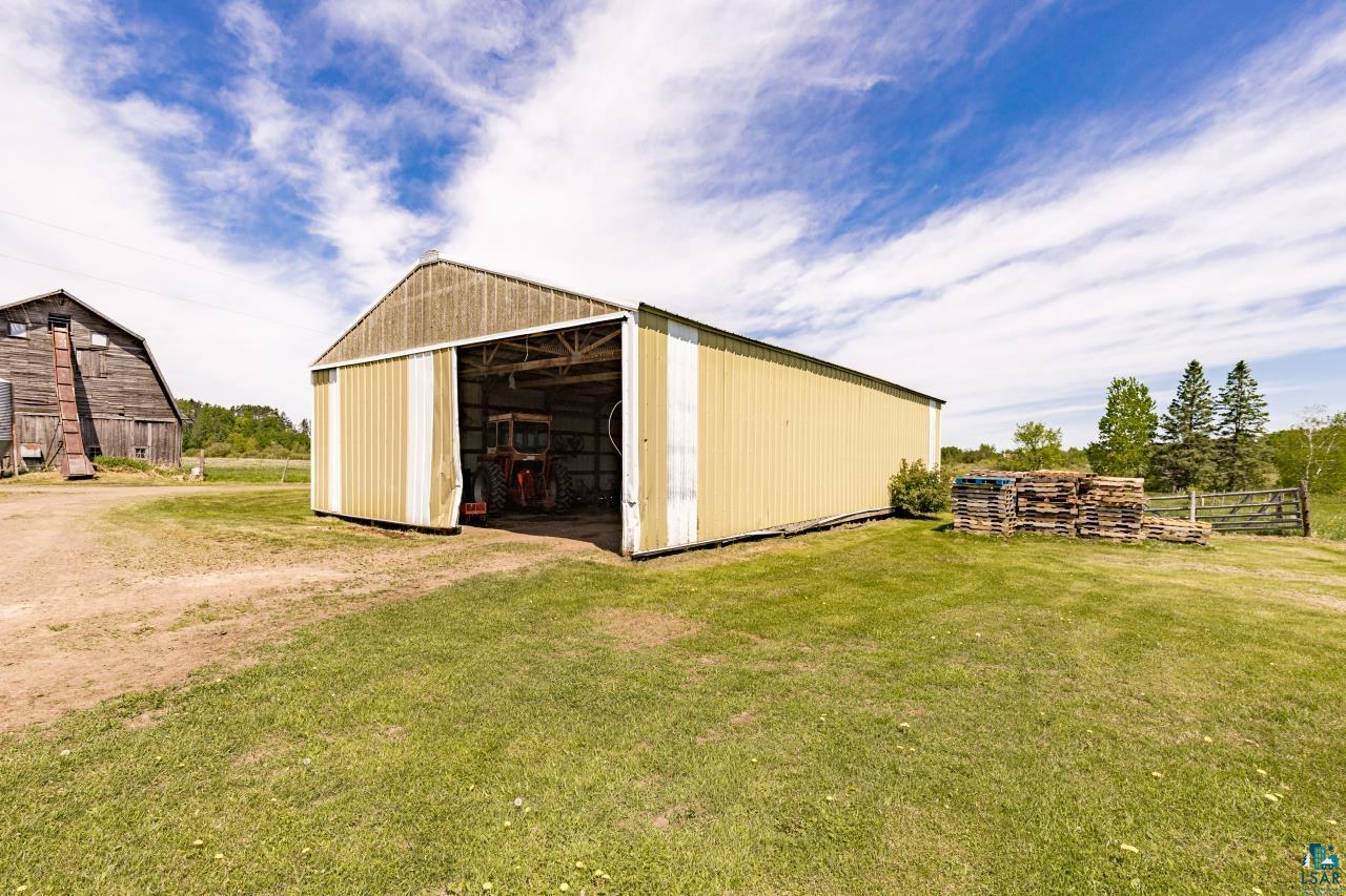 6606 Metso Road Kettle River, MN 55757 - Photo 69 of 84 Metal outbuilding with a gambrel-style roof, featuring a large sliding door, a dirt driveway, and a grass area