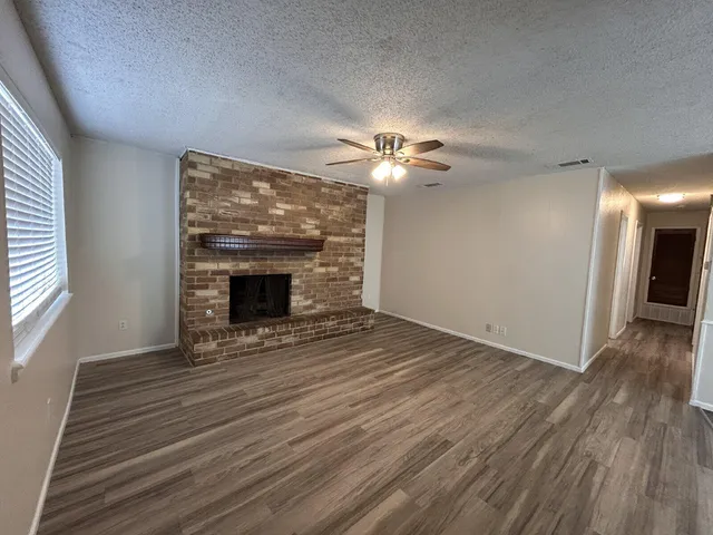 a view of an empty room with wooden floor fireplace and a window