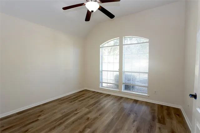an empty room with wooden floor fan and windows