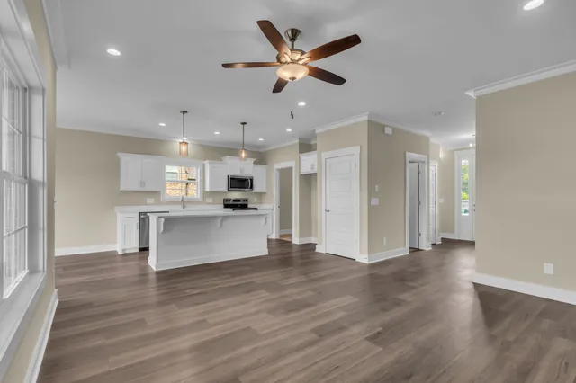a view of an empty room and kitchen with wooden floor