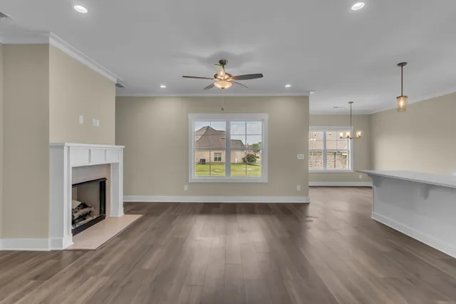 an empty room with wooden floor a ceiling fan a fireplace and windows