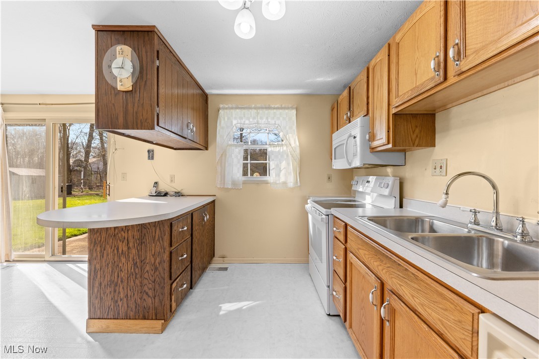 4301 Baird Road Stow, OH 44224 - Photo 15 of 50 Kitchen with light countertops, a sink, white appliances, baseboards, and a peninsula
