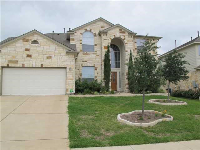 View of front of property featuring a front yard, driveway, an attached garage, and stone siding