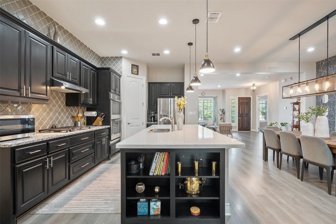 225 Escarpment Way Cedar Park, TX 78613 - Photo 8 of 40 a kitchen with stainless steel appliances kitchen island granite countertop a table chairs sink and cabinets