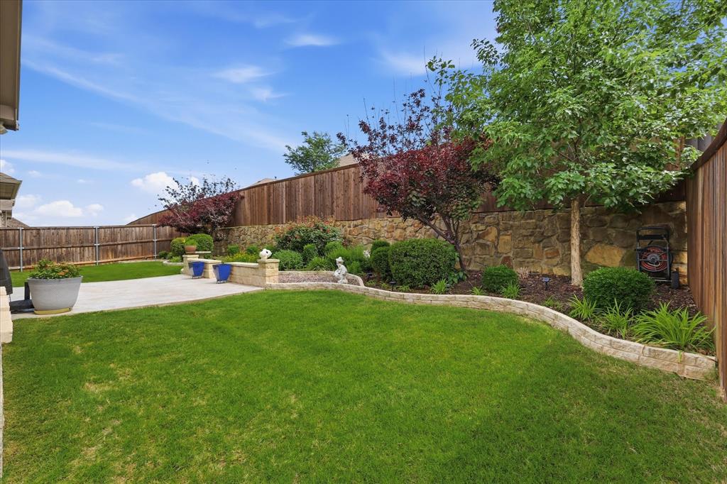 9708 Surveyor Road Oak Point, TX 75068 - Photo 34 of 34 Expansive backyard featuring a manicured lawn, a stone retaining wall, mature trees, a concrete patio, and privacy fencing