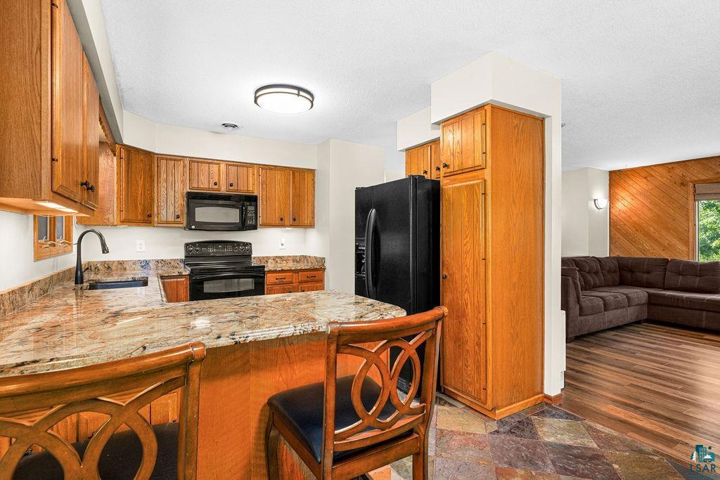 5370 Ugstad Road Hermantown, MN 55811 - Photo 33 of 68 Kitchen featuring wood cabinetry, black appliances, a stone-finish countertop, and a built-in breakfast bar
