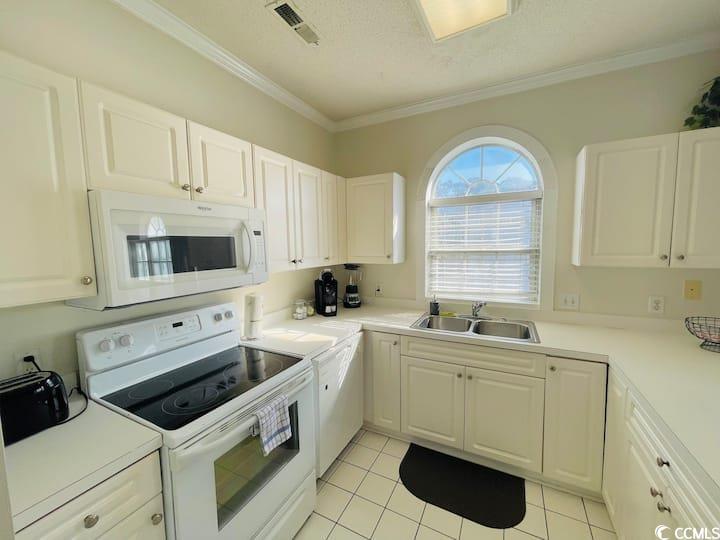 4631 Wild Iris Drive, Unit 301 Myrtle Beach, SC 29577 - Photo 12 of 37 Kitchen featuring white appliances, light countertops, white cabinets, crown molding, and light tile patterned flooring