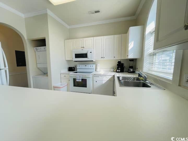 4631 Wild Iris Drive, Unit 301 Myrtle Beach, SC 29577 - Photo 14 of 37 Kitchen featuring light countertops, white appliances, arched walkways, estacked washer and dryer, and white cabinetry