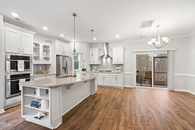 a kitchen with stainless steel appliances kitchen island granite countertop a large center island a stove a refrigerator cabinets and a wooden floor