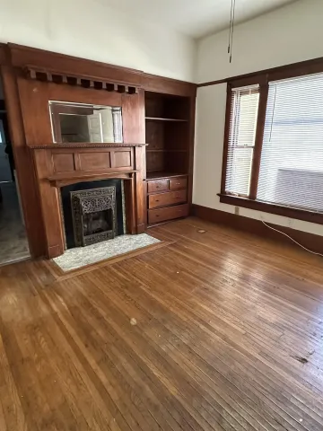 an empty room with wooden floor fireplace and windows