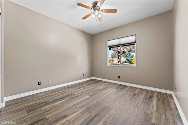 an empty room with wooden floor chandelier fan and windows