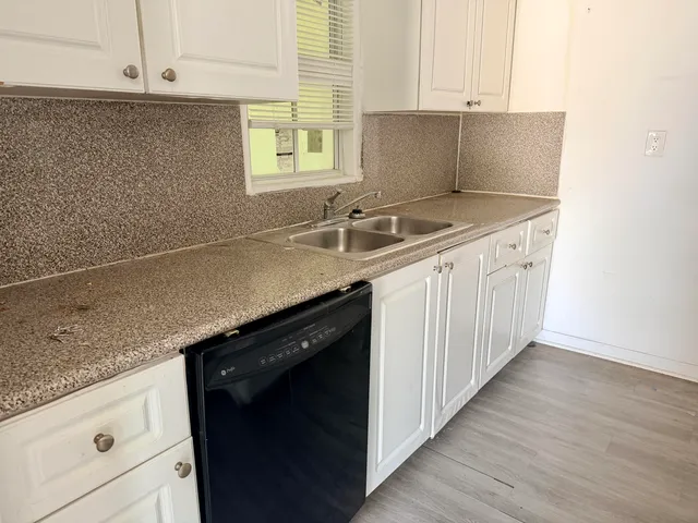 a kitchen with granite countertop a sink dishwasher a stove and white cabinets with wooden floor