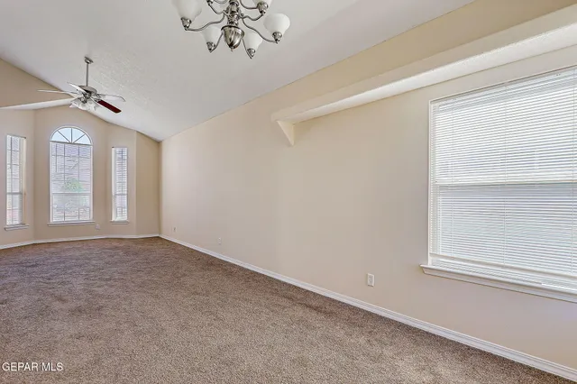 an empty room with chandelier fan and windows