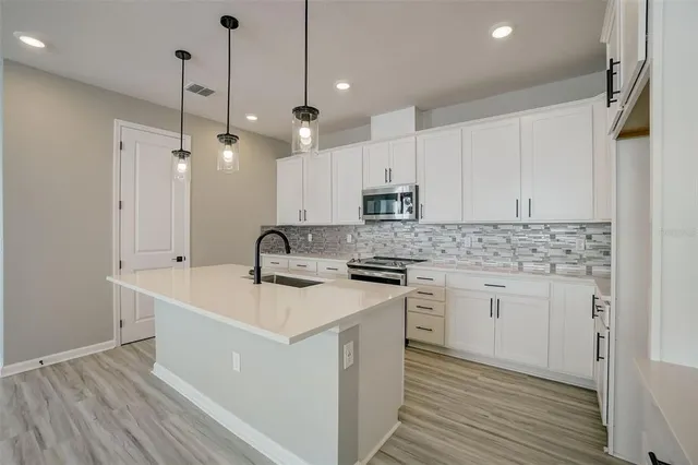 a kitchen with stainless steel appliances granite countertop a sink stove and white cabinets with wooden floor