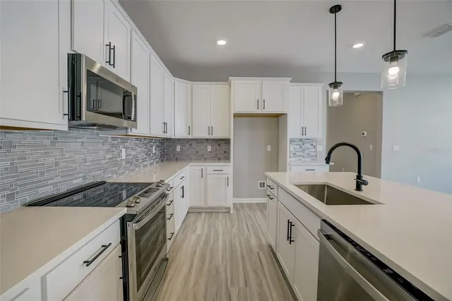 a kitchen with stainless steel appliances granite countertop a sink a stove top oven a refrigerator with white cabinets and wooden floor