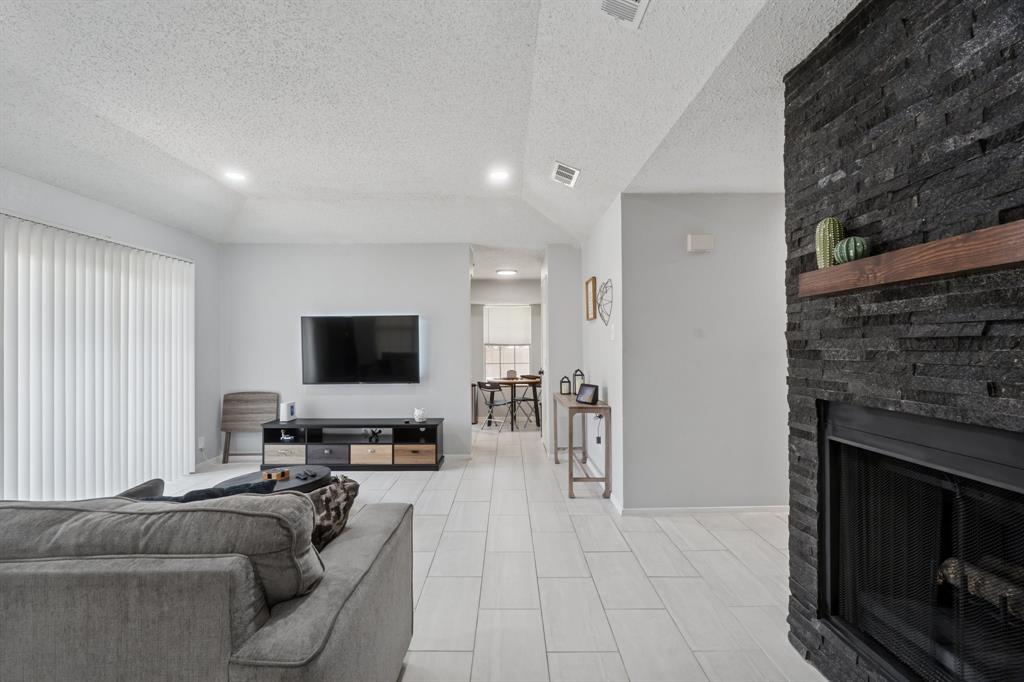 9780 Windy Ridge Road Frisco, TX 75033 - Photo 6 of 25 Living area featuring a black ledger stone fireplace with a wood mantle, light wood-finish flooring, and vertical blinds